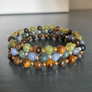 May include: A multi-strand bracelet with green, brown, blue, and gold beads. The bracelet is made of various gemstones and metal beads.