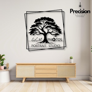 May include: A black metal wall sign featuring a silhouette of a large tree with a tyre swing hanging from a branch. The design is enclosed in two overlapping square frames. The text reads ELM PHOTOS PORTRAIT STUDIO in a clean, sans-serif font.