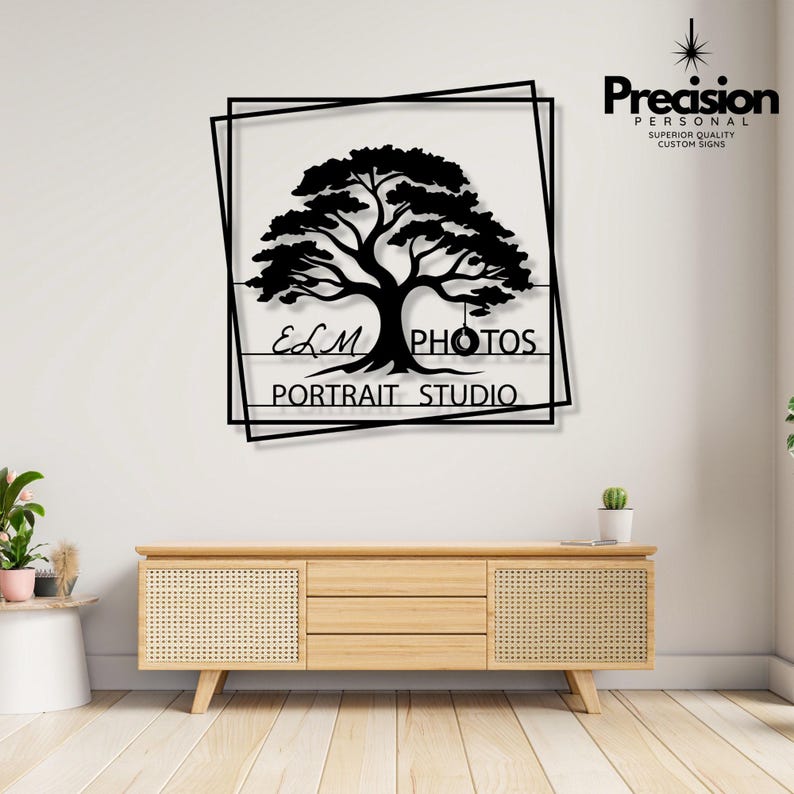 May include: A black metal wall sign featuring a silhouette of a large tree with a tyre swing hanging from a branch. The design is enclosed in two overlapping square frames. The text reads ELM PHOTOS PORTRAIT STUDIO in a clean, sans-serif font.