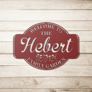 May include: Red metal sign with the text "Welcome to the Hebert Family Garden" in a white, decorative font. The sign has a rounded shape with a floral design.