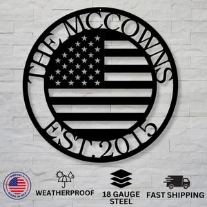 May include: Black metal wall art featuring the American flag design with the text "THE MCCOWNS EST. 2015" in a circular frame. The flag has white stars and black and white stripes. The art is made of 18 gauge steel.