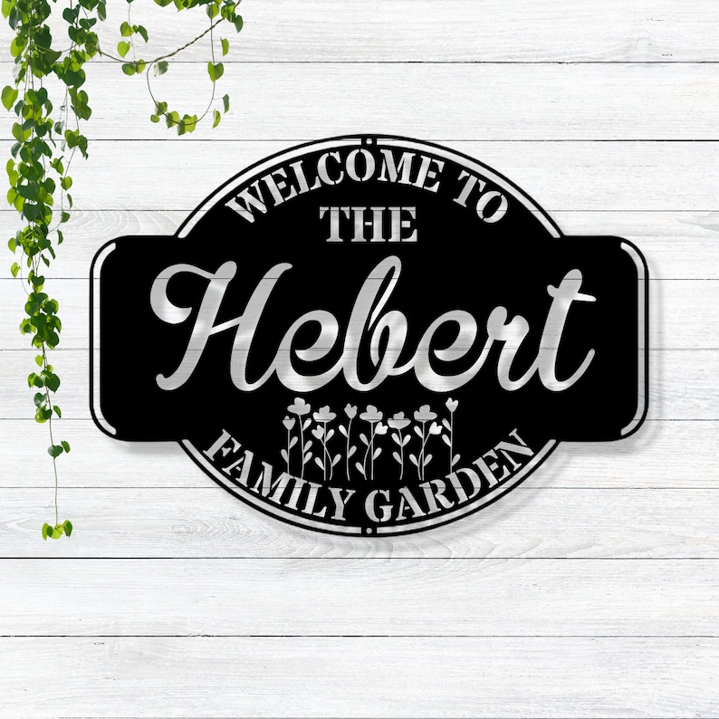 May include: Black metal sign with white lettering that reads "Welcome to the Hebert Family Garden".