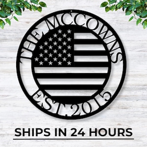 May include: Black metal wall art featuring the American flag design with the text "THE MCCOWNS EST. 2015" in a circular frame. The flag includes white stars and stripes. The art is suitable for indoor or outdoor display.
