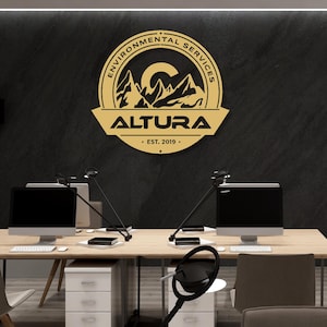 May include: A gold-colored sign with the text "ENVIRONMENTAL SERVICES" in a circular design, and "ALTURA" below it. The sign also includes the text "EST. 2019." The sign is mounted on a black wall above a desk with two computer monitors.