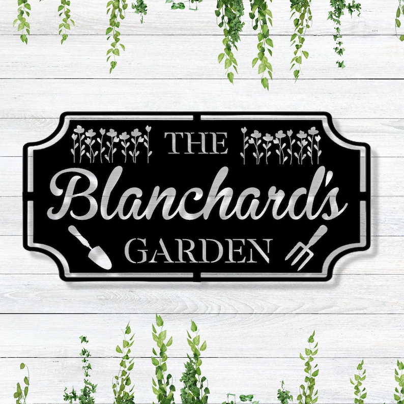 K&ouml;nnte beinhalten: Schwarzes Garten Schild aus Metall mit silberner Beschriftung "The Blanchard's Garden". Das Schild hat einen dekorativen Rand mit einer Schaufel und einer Heugabel auf beiden Seiten des Textes.