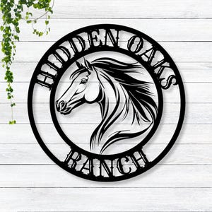 May include: Black metal sign with a horse head silhouette in the center. The sign reads "Hidden Oaks Ranch" in a decorative font.