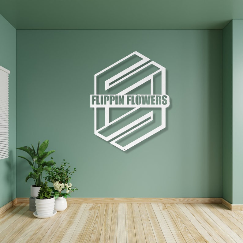 May include: White metal wall art with the text "FLIPPIN FLOWERS" in a geometric design. The art is mounted on a green wall above a wooden floor. Potted plants are in the foreground.