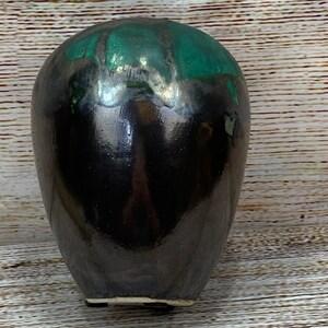 May include: A black ceramic vase with a glossy finish. The top of the vase has a green glaze. The vase has a rounded shape and a slightly textured surface. The base of the vase is a lighter color.