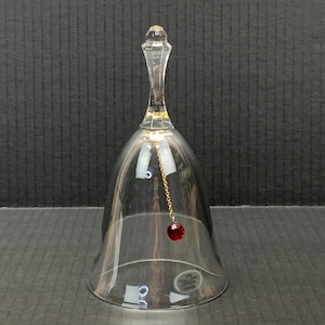 Peut inclure: Une cloche en cristal transparent avec une longue et fine poignée et un pendentif en cristal rouge rond suspendu à l'intérieur. La cloche a une forme classique et une chaîne dorée. La cloche est étiquetée "24% FULL LEAD CRYSTAL".