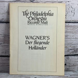 Puede incluir: Un programa vintage de Der fliegende Holländer de Wagner, con la Orquesta de Filadelfia y Riccardo Muti. La portada es de color crema con texto negro, incluyendo el nombre de la orquesta y el título de la ópera.