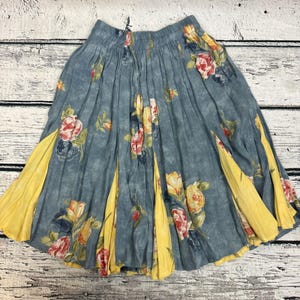 May include: A blue floral skirt with yellow panels. The skirt features a watercolor-style floral pattern in shades of red, yellow, and blue. The skirt is pleated and has a flowing silhouette.