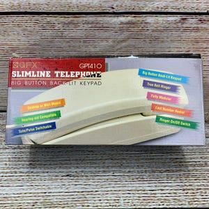 May include: A cream-colored slimline telephone with a big button back-lit keypad. The box features the text "SLIMLINE TELEPHONE" and "BIG BUTTON BACK-LIT KEYPAD". Additional features include "Desktop or Wall Mount", "Hearing-aid Compatible", and "Tone/Pulse Switchable".