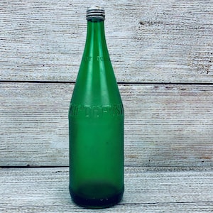 May include: A vintage green glass bottle with a silver cap. The bottle has the words "NO DEPOSIT" embossed on the side. The bottle is empty and has a long, slender neck.