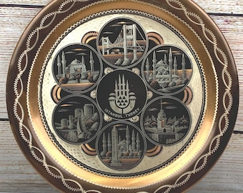 May include: Round copper-toned decorative tray featuring embossed images of Istanbul landmarks. The tray has a dark brown border with a decorative edge and a central emblem that reads "ISTANBUL TURKEY".
