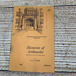 May include: A vintage book titled "Elements of Arithmetic" from 1975, with a detailed illustration of a building on the cover. The book is tan with black text and illustrations. The cover also includes the text "International Correspondence Schools Scranton, Pa."