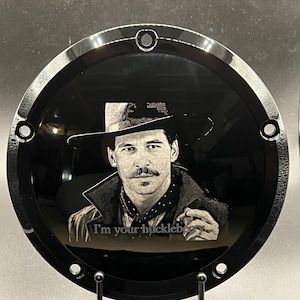 May include: Black motorcycle part with a portrait of a man in a hat and the text "I'm your huckleberry." The image is a detailed engraving on a glossy black surface, with a silver trim and mounting holes.