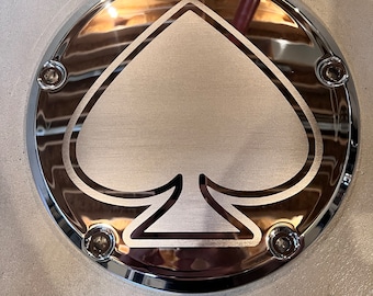May include: A chrome motorcycle cover with a silver spade design. The cover has six screws around the edge.