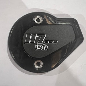 May include: Black, oval-shaped component with the text "117...ish" in white. The component has two circular holes and a textured center. The item appears to be made of a glossy material.