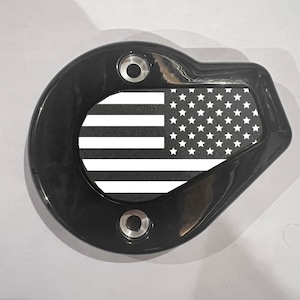 May include: A black, glossy, decorative cover with a design of the American flag. The cover has a rounded shape with two circular holes and a rectangular section displaying the flag's stars and stripes.