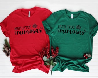 May include: Two t-shirts with the text "Mistletoe and mimosas" in black lettering on a red and green shirt.