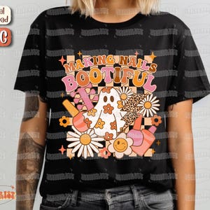 May include: Black t-shirt with a retro design that says "MAKING NAILS BOOTIFUL". The graphic includes a ghost, flowers, nail polish bottles, and a lightning bolt with a leopard print pattern. The design has a vintage, groovy aesthetic.