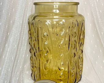 Pode incluir: Um pote vintage de vidro âmbar com um design em relevo floral e uma tampa de vidro transparente. O pote tem uma forma quadrada e é perfeito para guardar biscoitos, doces ou outras guloseimas.