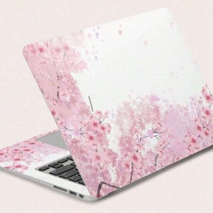 May include: A laptop with a pink floral design featuring cherry blossoms. The design covers the lid and the area around the keyboard. The blossoms are in shades of pink and red against a white background.