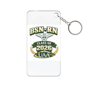 May include: A rectangular keychain with a silver chain and ring. The white surface features the text "BSN RN" above a caduceus symbol, "CLASS OF 2026", and "UAA" in green and gold. The keychain is a graduation gift.