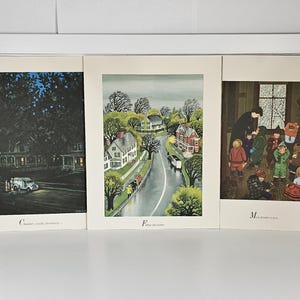 May include: Three matted art prints featuring illustrations. The left print shows a house at night with the text "C is for vanilla, strawberry...". The center print depicts a street scene with the text "F is for father". The right print shows children indoors with the text "M is for mother to wear".