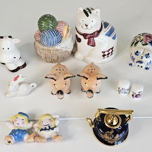 May include: A collection of ceramic figurines, including a cow, a rabbit, a cat, a pig, two pig-shaped salt and pepper shakers, two thimbles, two figurines of children, a basket of yarn, and a teapot.