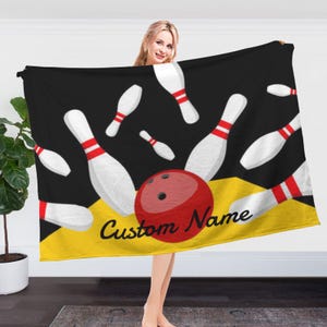 May include: A black and yellow fleece blanket with a bowling ball and bowling pins design. The text "Custom Name" is printed on the blanket.
