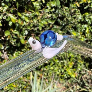 May include: A glass turtle figurine with a blue and white shell, sitting on a clear glass rod.