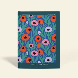 May include: A notebook with a floral pattern. The cover has a blue backdrop with orange, pink, and purple flowers and green leaves. The text "THOUGHTS IN BLOOM" is at the bottom. The notebook is labelled "PERSONALIZABLE".