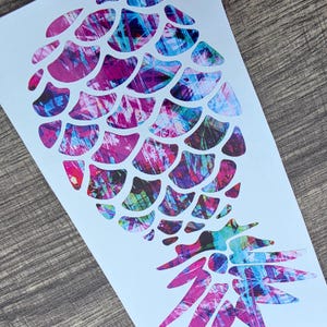 May include: A colourful pineapple sticker with an abstract design. The pineapple is made up of overlapping shapes in pink, purple, blue, and green, creating a textured effect. The sticker is on a white background.