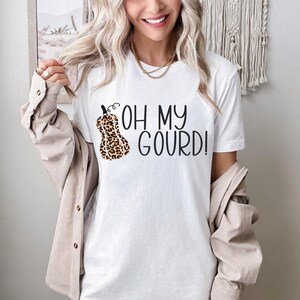 Puede incluir: Camiseta blanca con un gr&aacute;fico de calabaza de estampado de leopardo negro y marr&oacute;n y el texto "Oh My Gourd!"