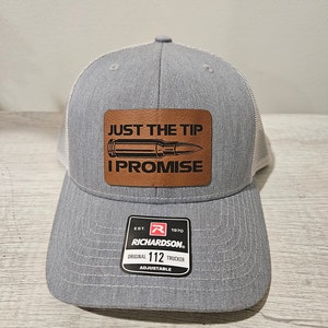 May include: A gray and white trucker hat with a brown leather patch that says "Just the Tip I Promise" with a black silhouette of a bullet. The hat has a red and white label that says "Est. 1970 Richardson Original 112 Trucker Adjustable".