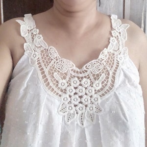 May include: White sleeveless top with a delicate lace overlay. The lace features a floral design and a scalloped edge.