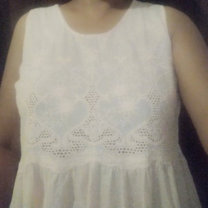 May include: White sleeveless dress with a delicate floral lace pattern around the neckline and bodice.