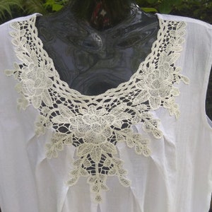 May include: White sleeveless top with a delicate lace trim around the neckline. The lace is a cream color and features a floral design.