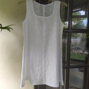 May include: White sleeveless dress with a delicate eyelet pattern. The dress has a scoop neckline and a loose, flowing silhouette.