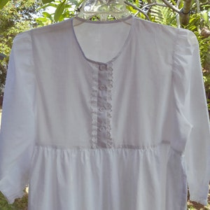 May include: A white long-sleeved dress with a lace trim down the front and a button closure. The dress has a gathered skirt and a slightly puffed sleeve.