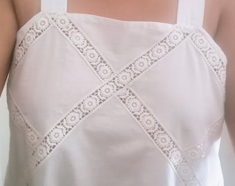 May include: White sleeveless top with a square neckline and a criss-cross lace design.