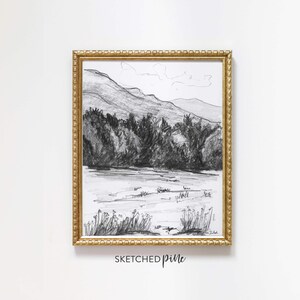 K&ouml;nnte beinhalten: Eine Schwarzwei&szlig;-Bleistiftzeichnung einer Berglandschaft mit einem See im Vordergrund. Die Zeichnung ist in einem goldenen Rahmen mit einem dekorativen Rand gerahmt. Der Text "SKETCHED pine" ist unter dem Rahmen gedruckt.