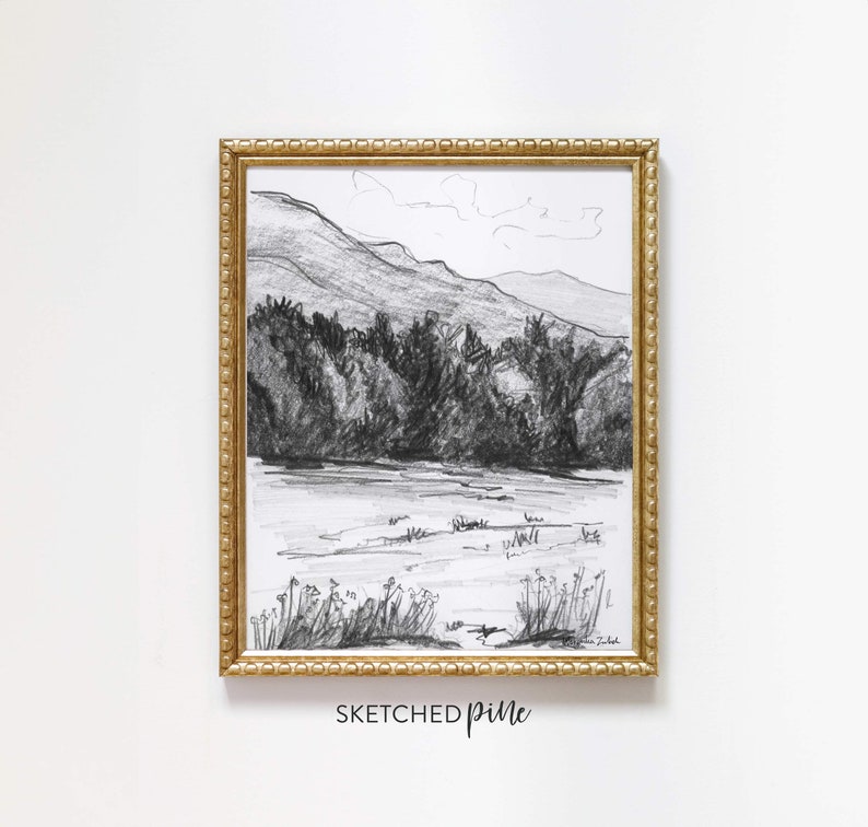 K&ouml;nnte beinhalten: Eine Schwarzwei&szlig;-Bleistiftzeichnung einer Berglandschaft mit einem See im Vordergrund. Die Zeichnung ist in einem goldenen Rahmen mit einem dekorativen Rand gerahmt. Der Text "SKETCHED pine" ist unter dem Rahmen gedruckt.
