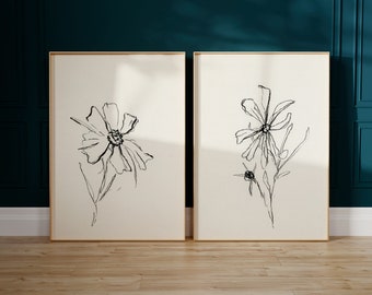 Puede incluir: Dos impresiones artísticas enmarcadas con dibujos lineales negros de flores sobre un fondo crema. La obra de arte se encuentra sobre una pared verde azulado y un suelo de madera, creando una estética minimalista. Los marcos son dorados.