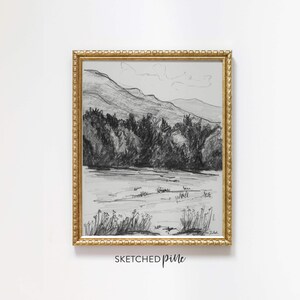 K&ouml;nnte beinhalten: Eine Schwarzwei&szlig;-Bleistiftzeichnung einer Berglandschaft mit einem See im Vordergrund. Die Zeichnung ist in einem goldenen Rahmen mit einem dekorativen Rand gerahmt. Der Text "SKETCHED pine" ist unter dem Rahmen gedruckt.