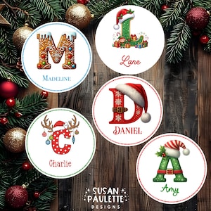 May include: Five circular Christmas-themed labels featuring letters M, L, D, C, and A. Each letter is decorated with holiday motifs like gingerbread, Santa hats, and reindeer antlers, accompanied by the names Madeline, Lane, Daniel, Charlie, and Amy.