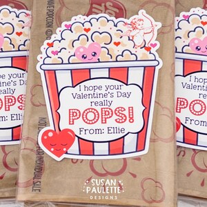 Puede incluir: Bolsas de golosinas de palomitas de ma&iacute;z para el D&iacute;a de San Valent&iacute;n con un dise&ntilde;o de contenedor de palomitas de ma&iacute;z a rayas rojas y blancas. Las bolsas tienen una pegatina que dice "&iexcl;Espero que tu D&iacute;a de San Valent&iacute;n realmente EXPLOTE!" con un coraz&oacute;n e ilustraci&oacute;n de cupido. De Ellie.