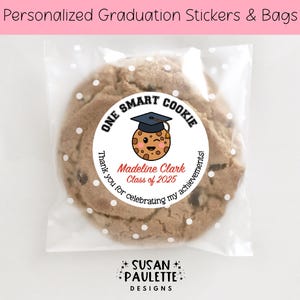 May include: A white round sticker with black text that reads "One Smart Cookie" and a cartoon cookie wearing a graduation cap. The sticker is on a clear plastic bag with a brown cookie inside. The text "Madeline Clark Class of 2025" is in red. The text "Thank you for celebrating my achievements!" is in black. The text "SUSAN PAULETTE DESIGNS" is in black.