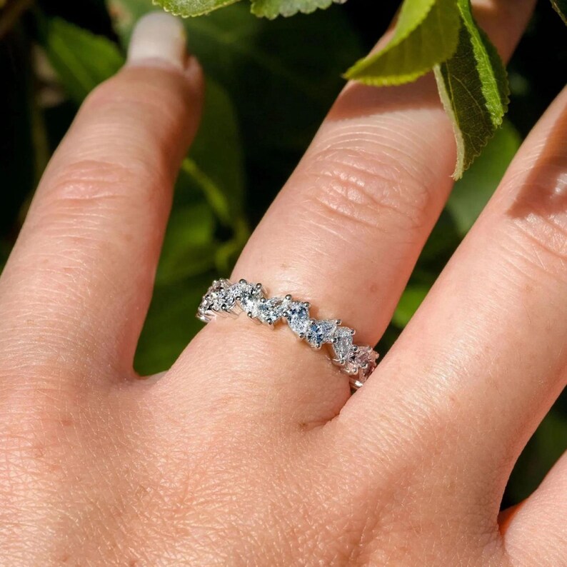 May include: A silver band ring with a row of small, clear, triangular-shaped stones.
